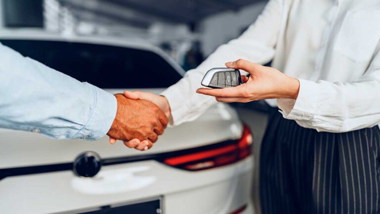 Imagem de um homem e uma mulher se cumprimentando com aperto de mãos e entregando uma chave canivete. Um carro branco ao fundo. vender carro pessoa física